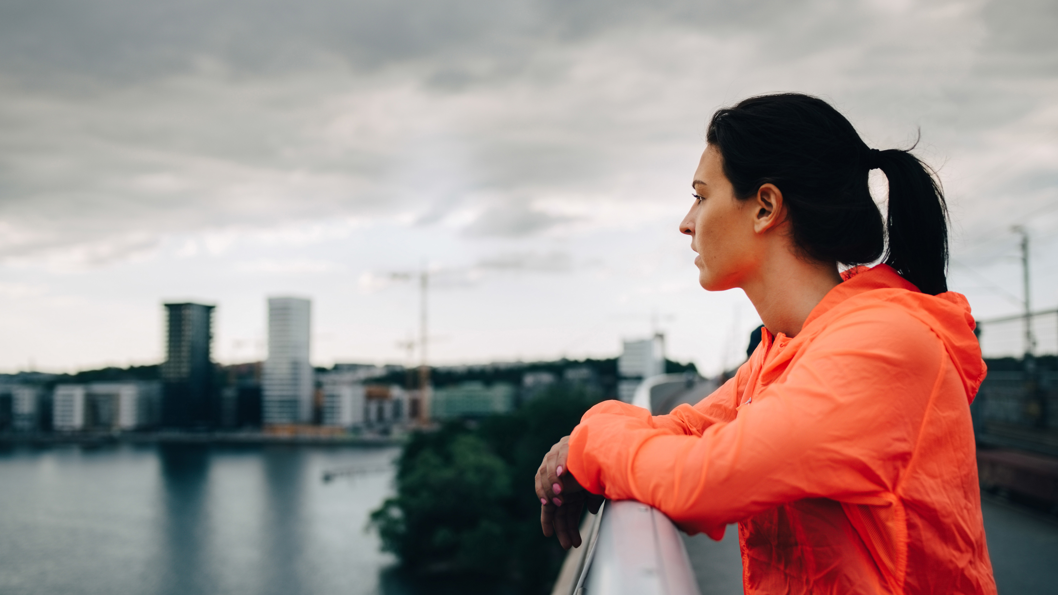 En kvinna står vid ett broräcke och blickar ut över en stad
