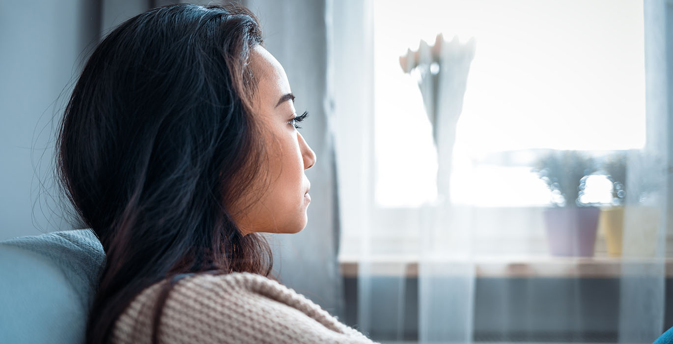 En kvinna sedd från sidan sitter och tittar ut genom fönstret.